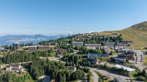 A town with a mix of modern and traditional buildings, surrounded by dense forests and mountains in the background. - Unusual chalet, 2 ppl, terrace with mountain view. (Chamrousse)
