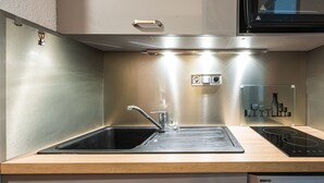A kitchen with a stainless steel sink, a stove, and a cabinet above.