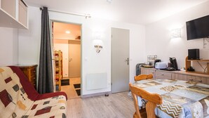 A compact room with a bed, a dining table, a TV, and a kitchenette.
