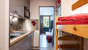 A compact room with a kitchenette, a bed, and a view through an open door.