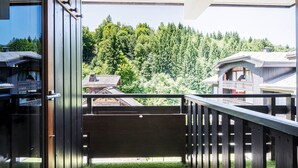 A wooden balcony with a view of a forested area and traditional buildings.