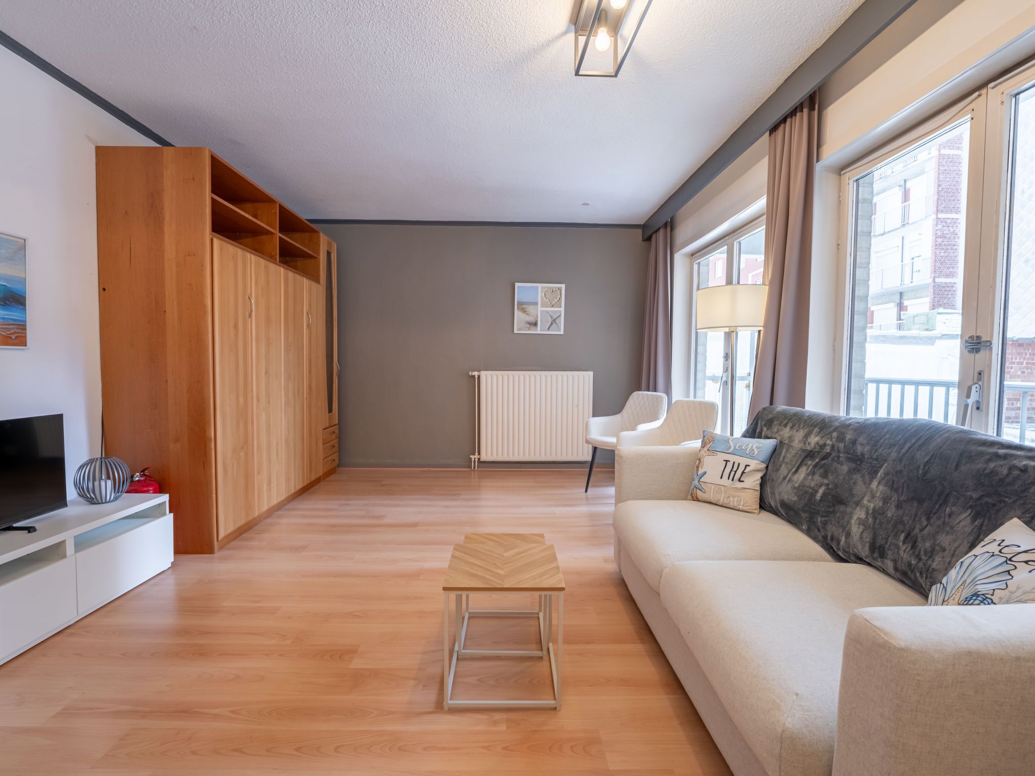 Un salon moderne avec un canapé, une petite table en bois, un téléviseur et une armoire.