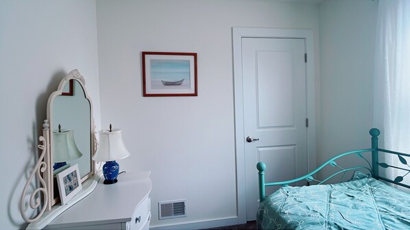 A bedroom with a white dresser, a mirror, a framed picture, a teal bed, and a white door.