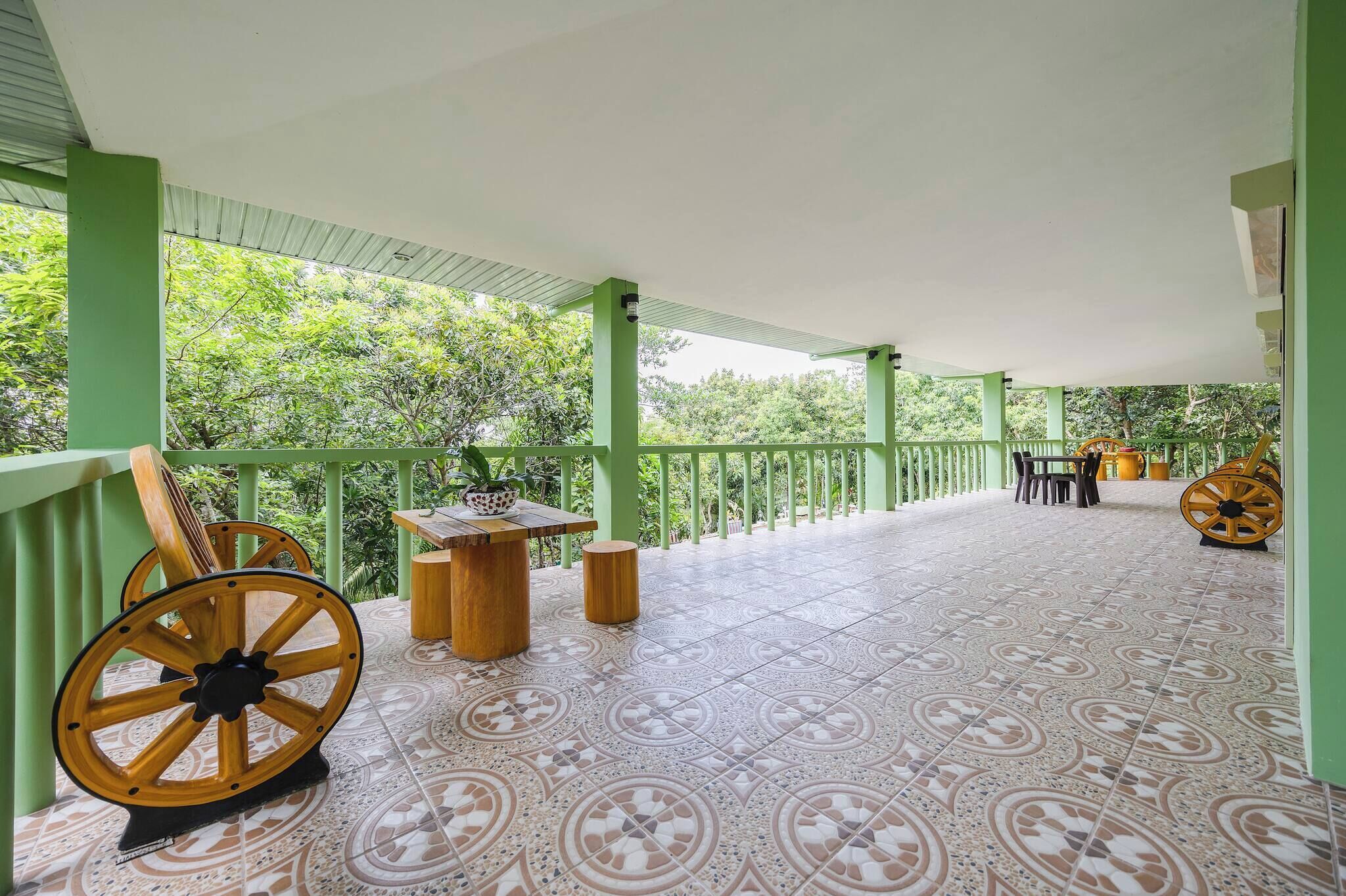 Un espacio al aire libre cubierto con piso de baldosas, barandas verdes, una mesa con sillas y una rueda de madera grande.