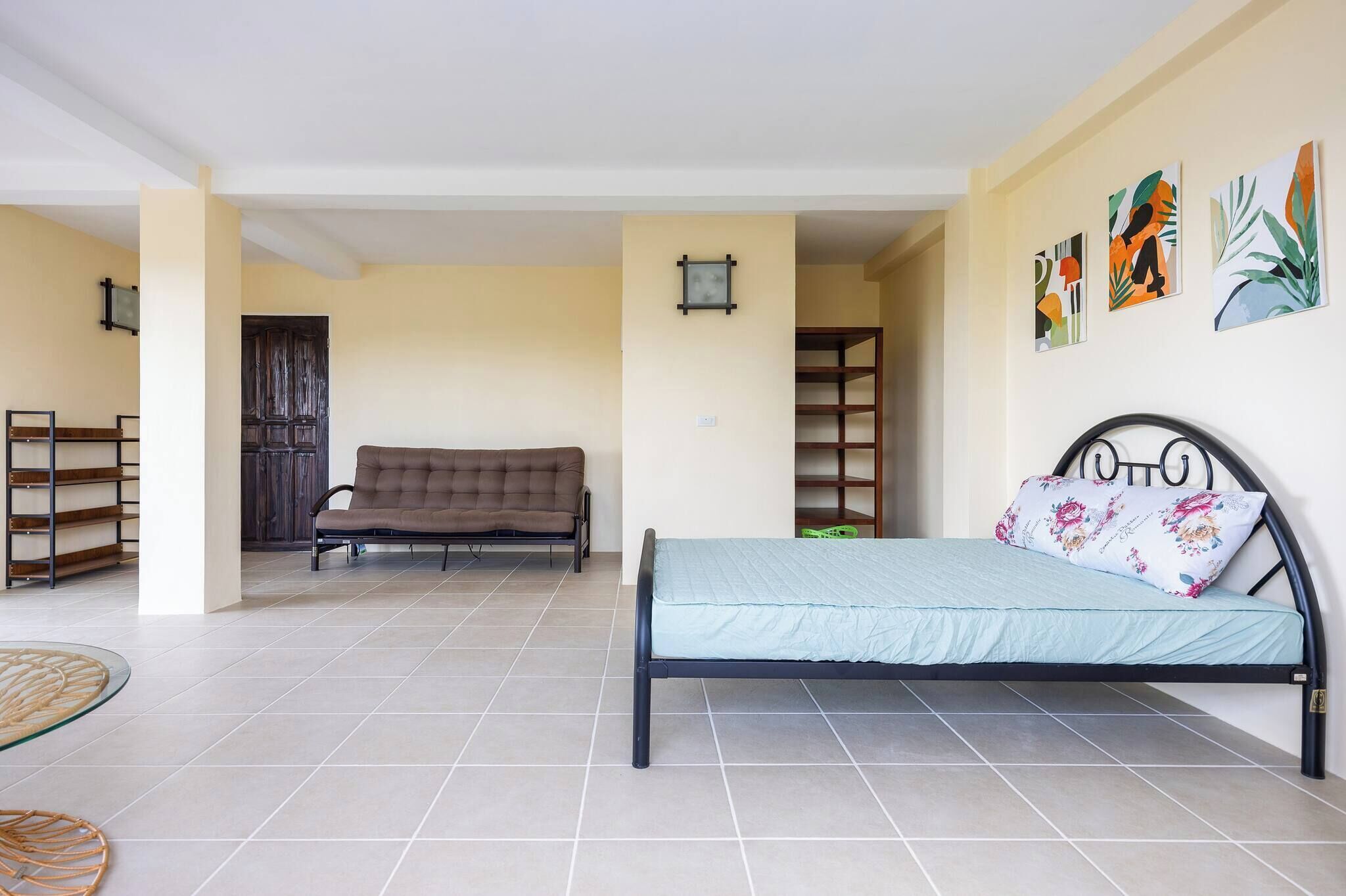 A bedroom with a bed, a sofa, and a chair. There are shelves and a door in the background.