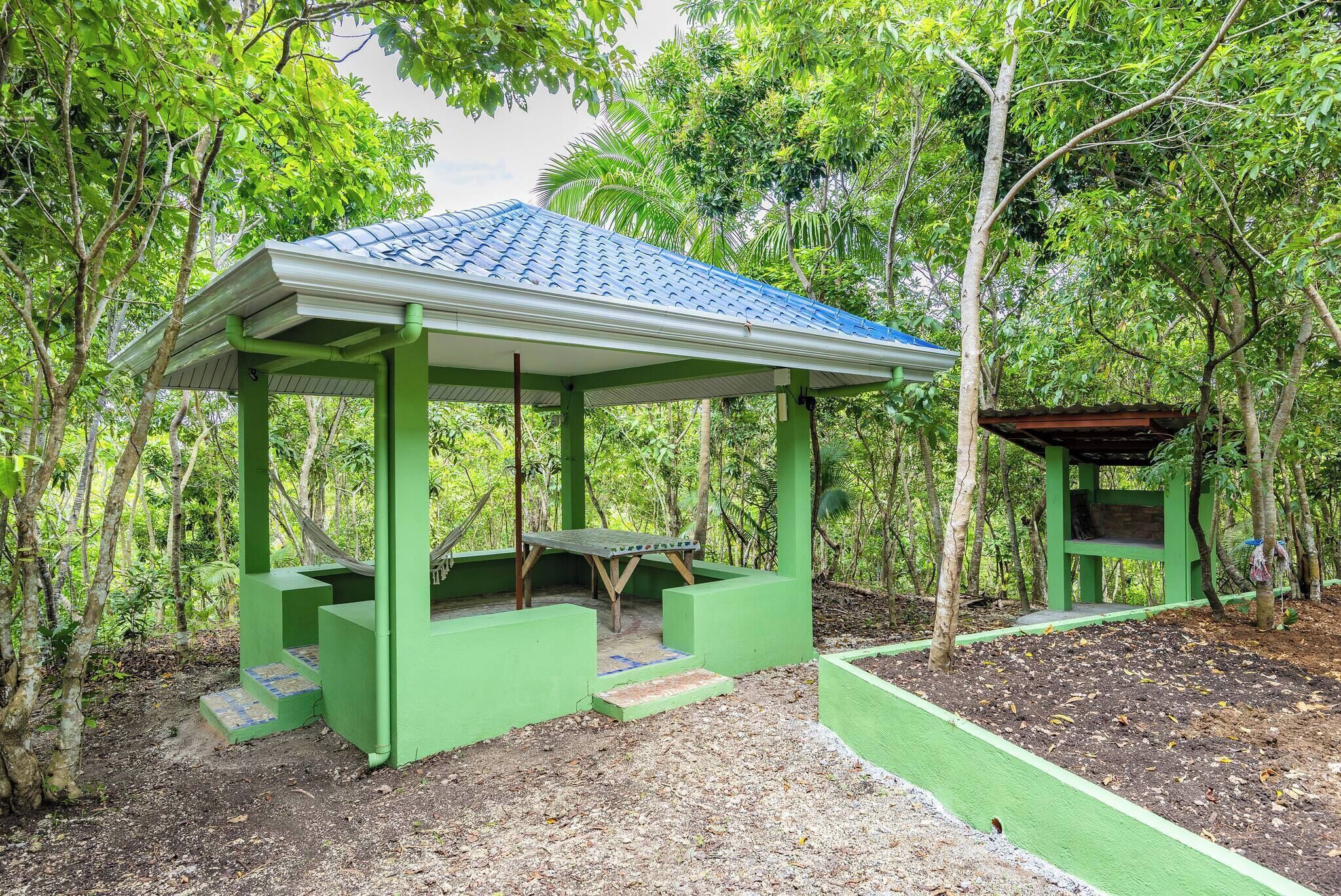 A green gazebo with a tiled roof, surrounded by trees.
