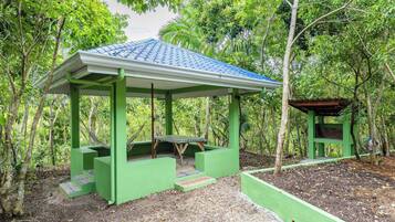 A green gazebo with a tiled roof, surrounded by trees.