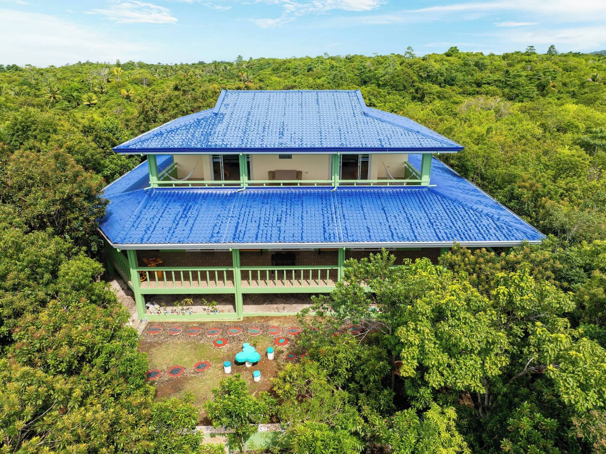Un edificio de dos plantas con techo azul, rodeado de abundante vegetación.
