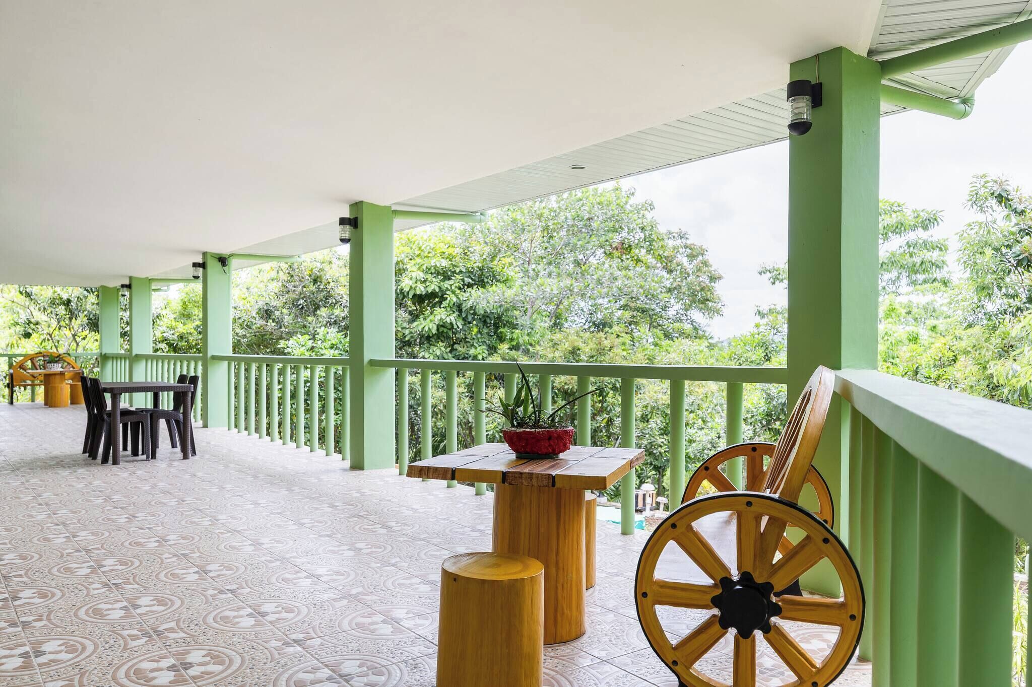 A covered outdoor area with a green railing, a wooden table with chairs, and a potted plant.