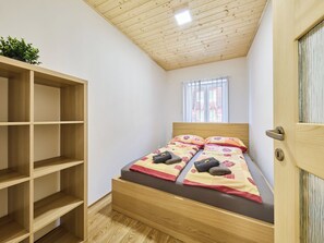 A bedroom with a wooden bed, a built-in wardrobe, and a window with blinds. - U Dzina by Interhome (Desná v Jizerských horách)