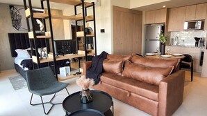 A modern living room with a brown leather sofa, a black chair, and a round coffee table. There is a kitchen area with a refrigerator and a microwave. - New apartment with beautiful views in Lomas del Country (Guadalajara)