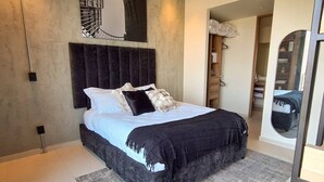 A modern bedroom with a large bed, dark headboard, and a mirror reflecting a bed and wardrobe. - New apartment with beautiful views in Lomas del Country (Guadalajara)