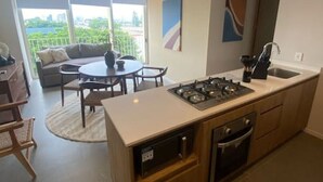 Une cuisine moderne équipée d’une cuisinière à gaz, d’un four et d’un évier, un coin repas avec une table ronde et des chaises, et un balcon offrant une vue sur la ville.