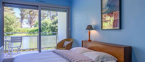 A bedroom with a bed, a chair, a table, a lamp, and a painting on the wall.