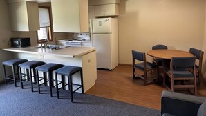 A compact kitchen with a stove, sink, and refrigerator, a small dining table with chairs, and a bar stool area. - Apartment Centrally Located (Plymouth)