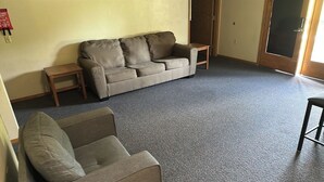 A living room with a grey carpet, a beige sofa, a wooden coffee table, and a small stool. - Apartment Centrally Located (Plymouth)
