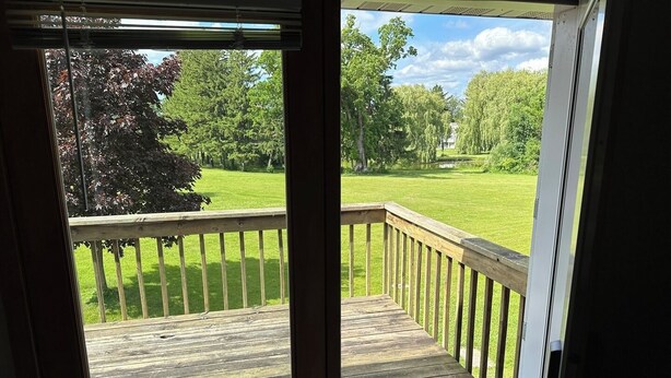 A wooden deck with a railing, leading to a grassy yard with trees and a clear sky. - Apartment Centrally Located (Plymouth)