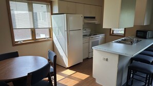 A compact kitchen with a refrigerator, stove, microwave, and a small dining area with a table and chairs. - Apartment Centrally Located (Plymouth)