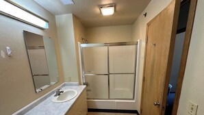 A bathroom with a white sink, a mirror, a shower with a glass door, and beige walls. - Apartment Centrally Located (Plymouth)