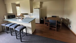Een kleine keuken met een centraal eiland, een magnetron, een spoelbak en een koelkast. Er staan vier barkrukken en een ronde tafel met stoelen.