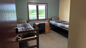 A small, single-room dormitory with two beds, a desk, and a window providing a view of the outdoors. - Apartment Centrally Located (Plymouth)