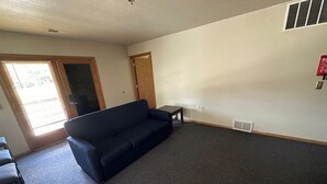 A living room with a dark blue sofa, a small table, and a chair. There is a door with a window, a vent on the wall, and a fire extinguisher mounted on the wall. - Apartment Centrally Located (Plymouth)