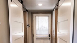 A hallway with a wooden floor, a white door with a window, and a black handle.