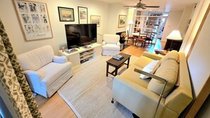 Ein Wohnzimmer mit Flachbildfernseher, weißen Sofas, einem Couchtisch und einem Bücherregal.
