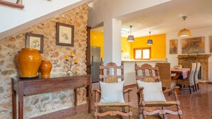 A dining area with wooden chairs and a table, a stone wall with framed pictures, and a kitchen in the background. - SON FIGUEROLA - Beautiful villa with private pool and free Wi-Fi in Inca (Inca)