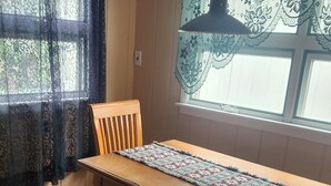 A dining area with a wooden table and chairs, a patterned rug, and a window with lace curtains. - Upper floor of charming 2 story house in central Hawley with WiFi (Hawley)