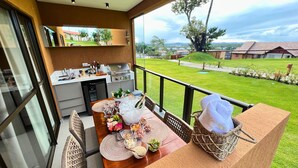 A balcony with a dining table set for four, a grill, and a view of a well-maintained lawn and distant buildings. - ECO RESORT | Carneiros Beach Right on the sand next to the Carneiros Church (Tamandaré)