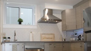 A modern kitchen with stainless steel appliances, wooden cabinets, and a wooden floor.