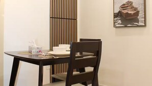 A dining area with a round table, two chairs, a wall-mounted light fixture, and a framed picture of a boat on water.