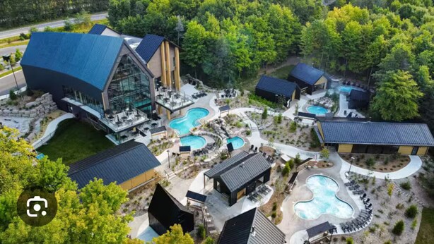 A resort with multiple swimming pools, a large glass building, and a forested backdrop.
