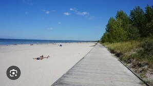 A beach with a wooden boardwalk, sandy beach, and trees in the background.