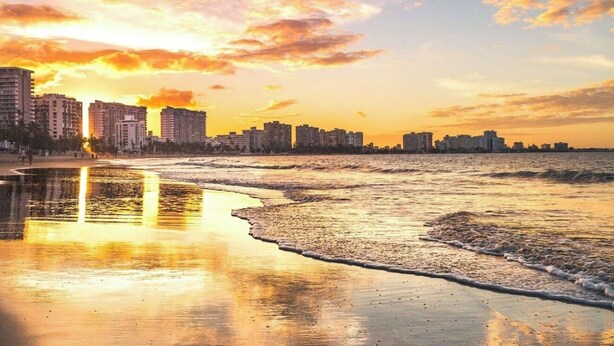A beach with a city skyline in the background during sunset.