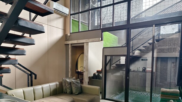 A modern living room with a staircase, a sofa, and a kitchen area. - Ohana Suites Yogyakarta (Yogyakarta)