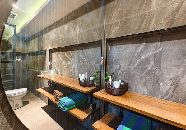 A modern bathroom with a marble wall, a glass shower enclosure, wooden benches, and a toilet.