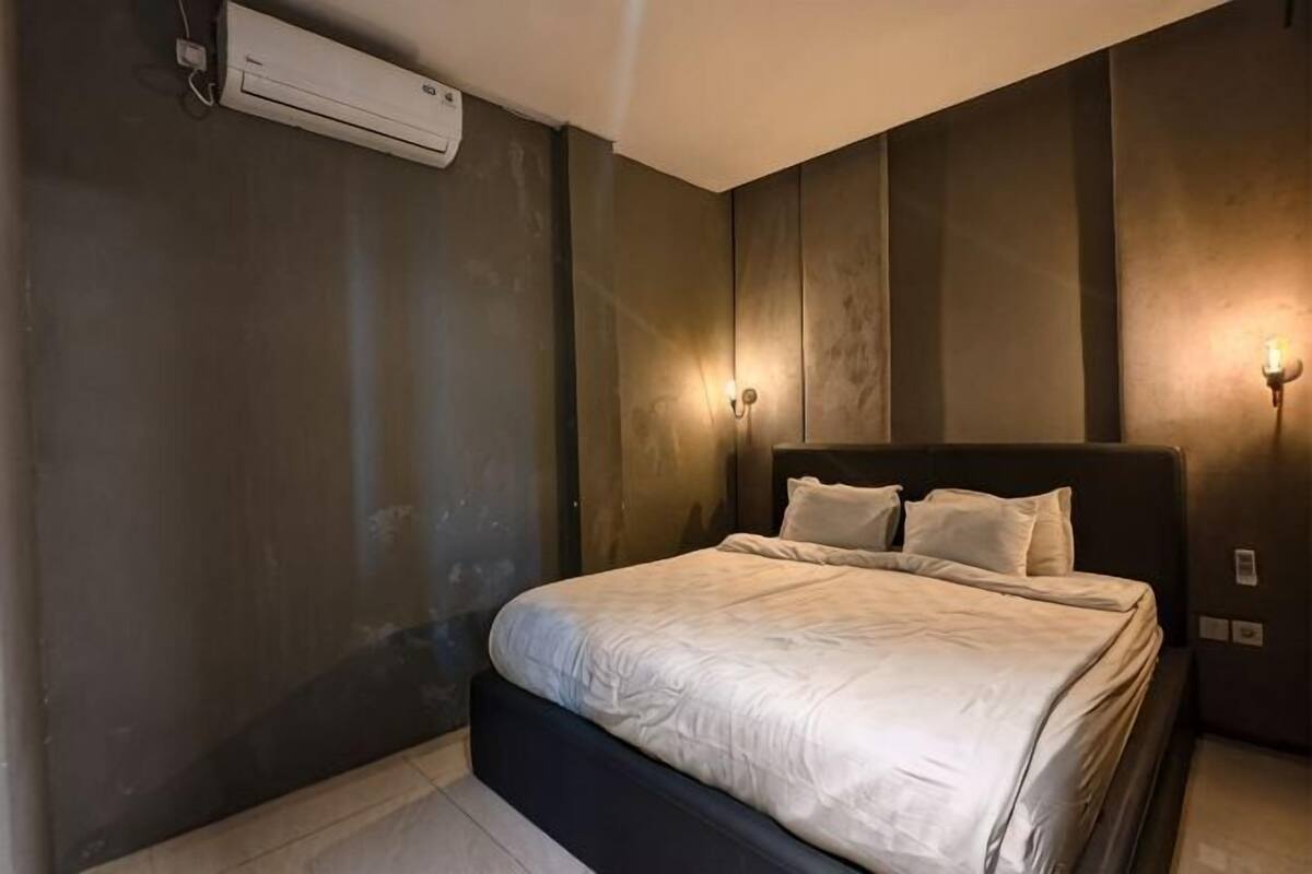 A bedroom with a bed, an air conditioner, and wall-mounted lighting.