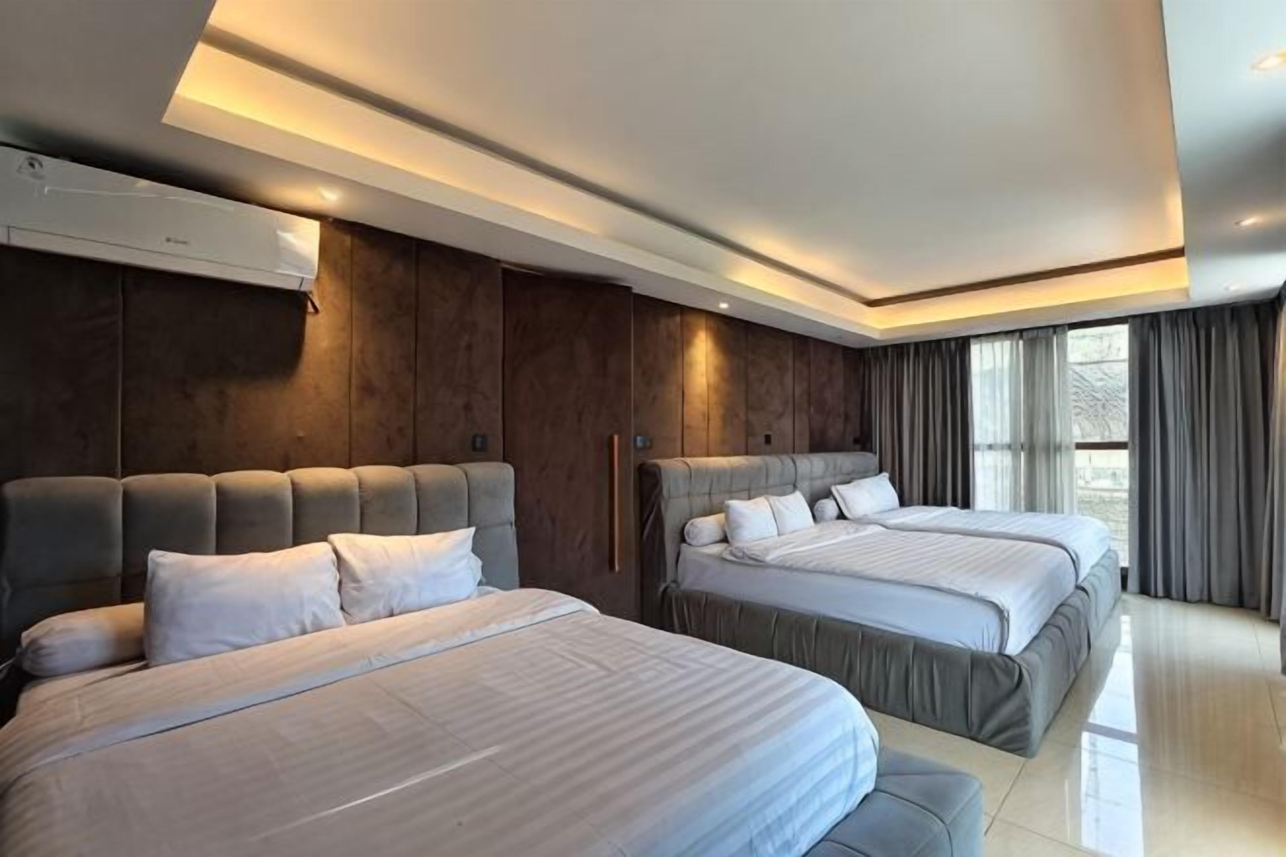 A modern hotel room with two beds, a large window, and a built-in air conditioning unit.