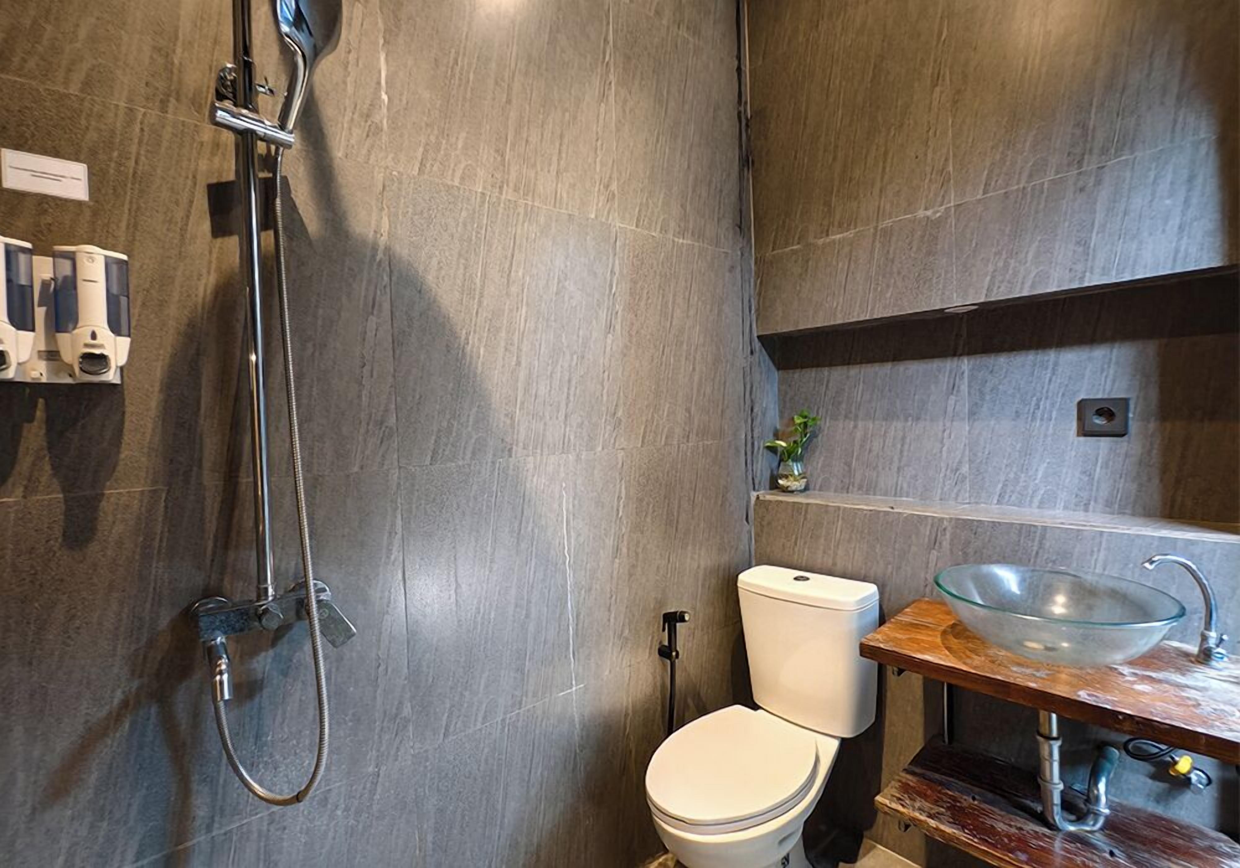 A modern bathroom with a shower, toilet, and a glass bowl sink.
