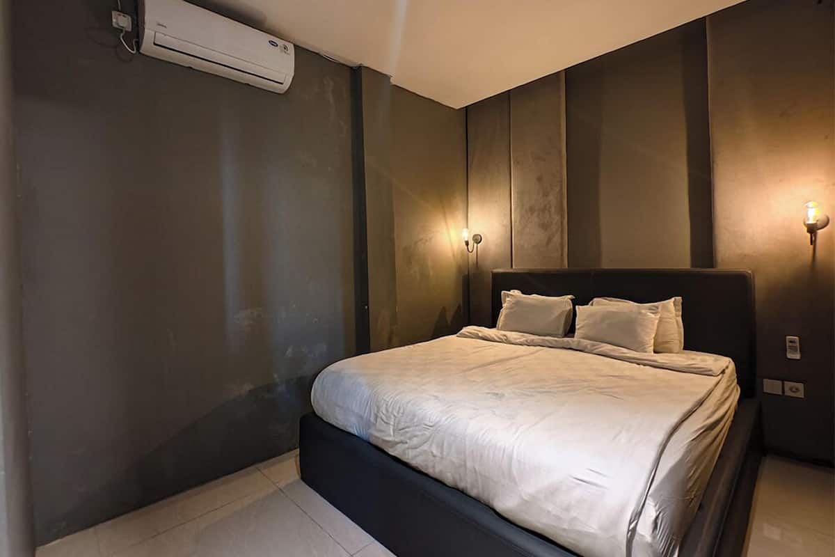 A modern bedroom with a large bed, an air conditioning unit, and wall-mounted lighting.