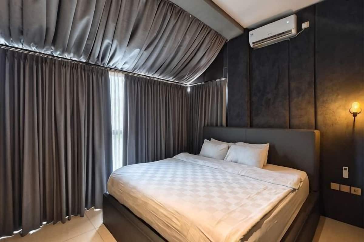 A modern hotel room with a large bed, dark walls, and a ceiling-mounted air conditioner.