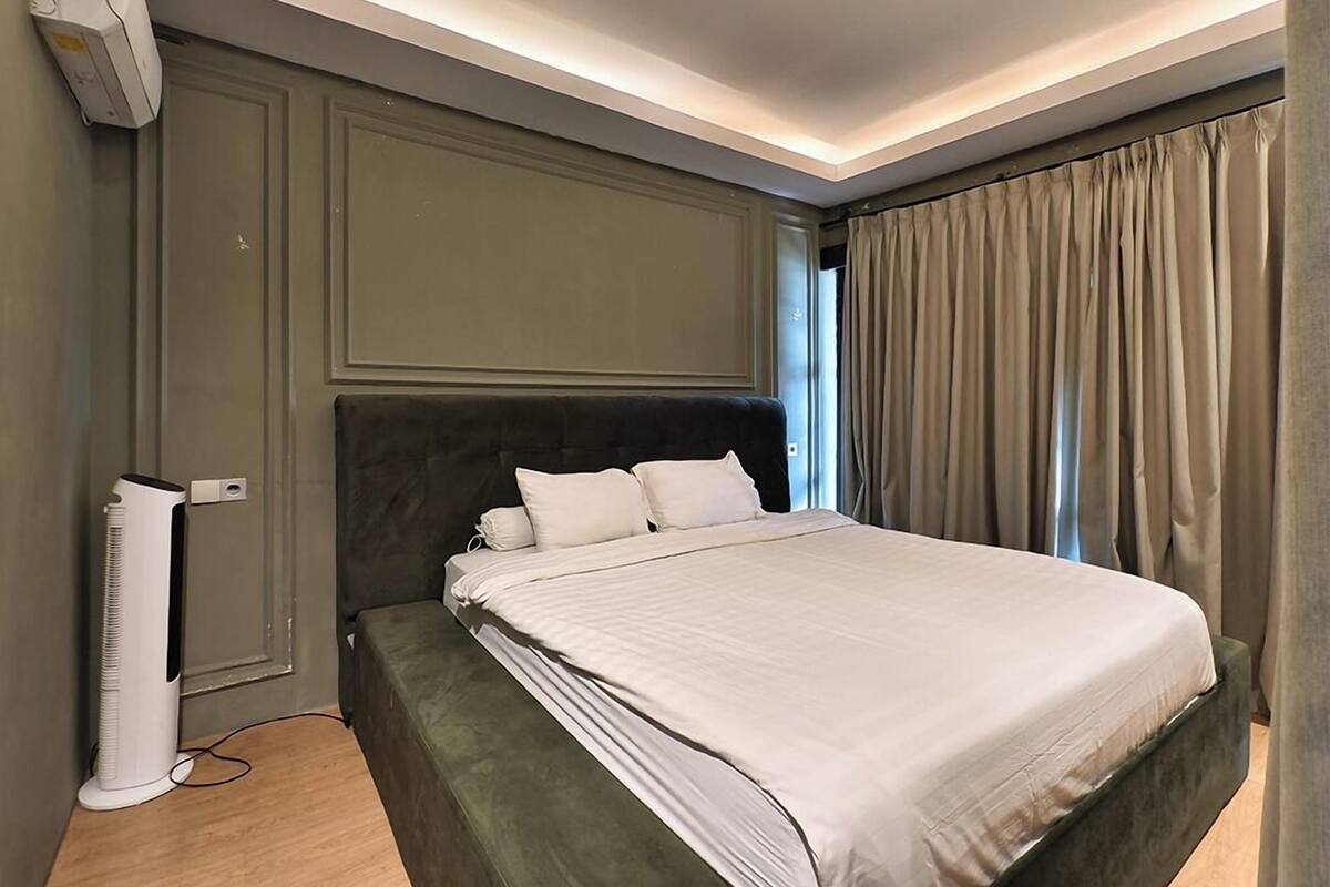 A modern bedroom with a large bed, a dark headboard, and a standing heater.