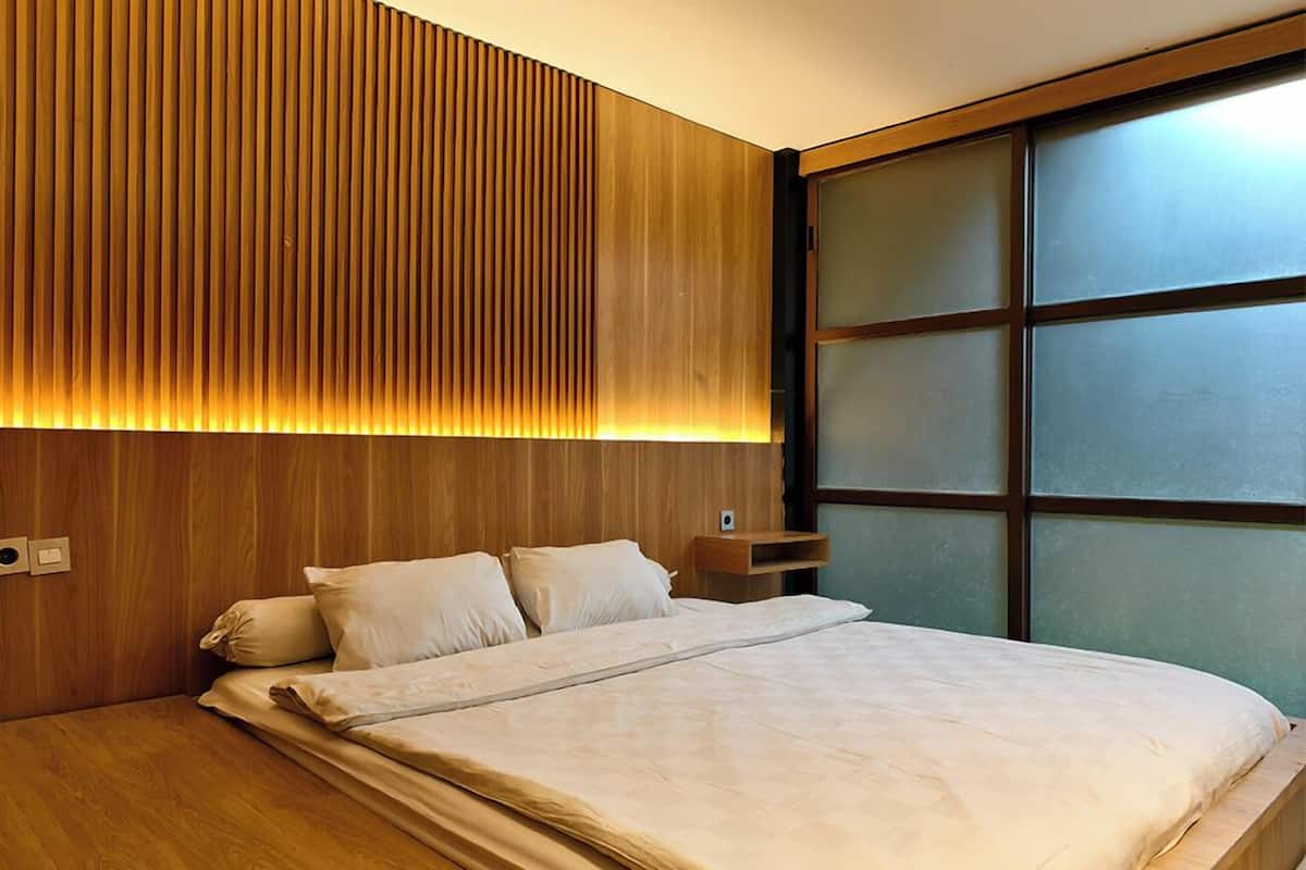 A modern bedroom with a wooden headboard, a large window, and a neatly made bed.
