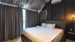 A modern hotel room with a large bed, dark walls, and a window with curtains. - Ohana Suites Yogyakarta (Yogyakarta)