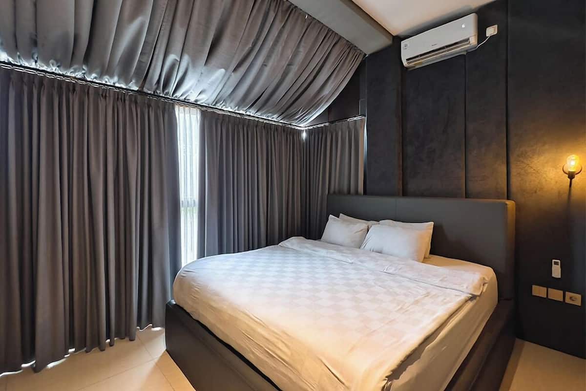 A modern hotel room with a large bed, dark walls, and a window with curtains.