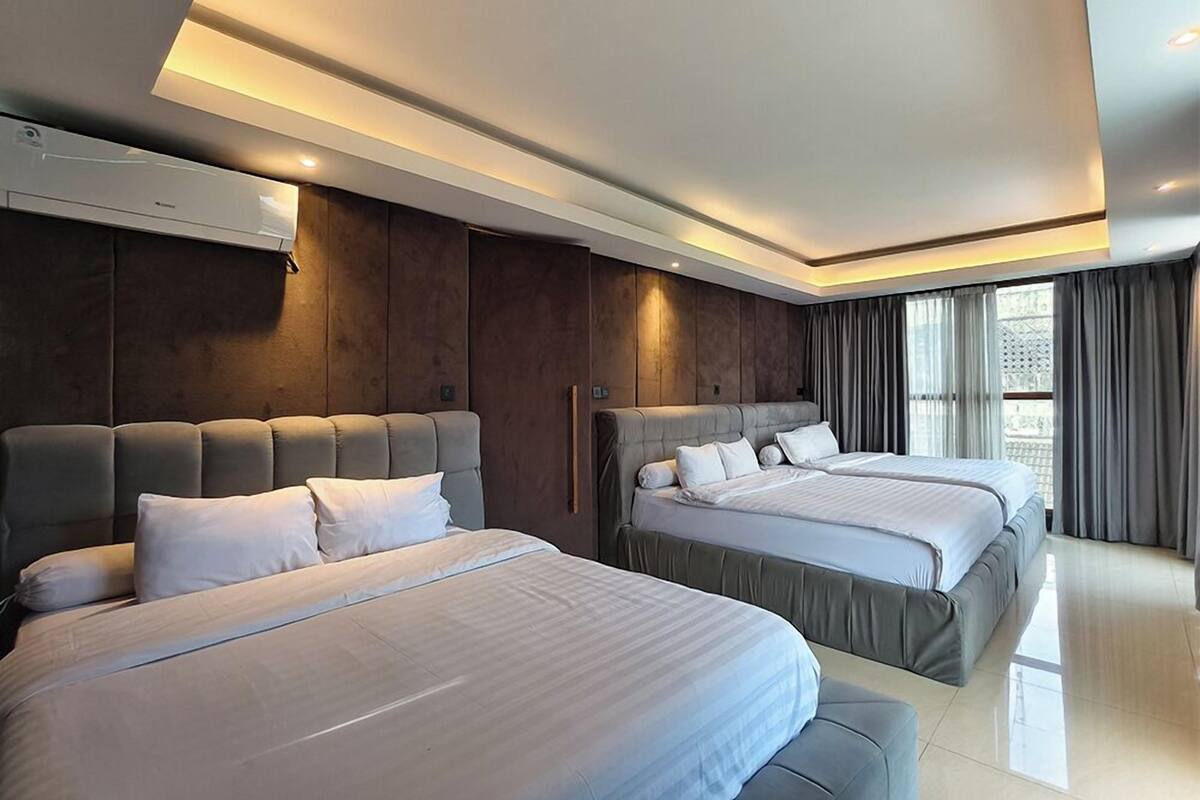 A modern hotel room with two beds, a large window with curtains, and an air conditioning unit on the wall.