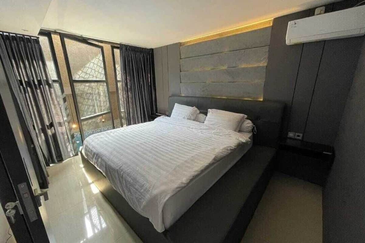 A modern bedroom with a large bed, a built-in headboard, and a window with curtains.