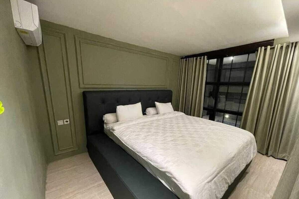 A bedroom with a bed, a bench, a window with curtains, and a wall-mounted air conditioner.